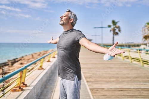 Middle age hispanic man wearing sportswear breathing at seaside