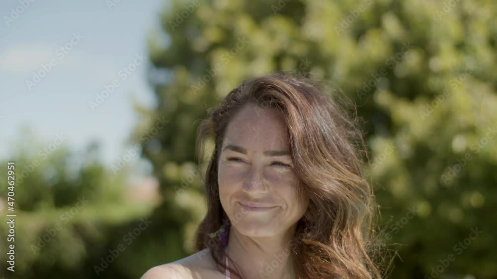 Close-up of smiling woman in bikini clinking glass into camera. Portrait of attractive girl drinking beverage with straw during summer party in backyard, communicating with friends. Emotion concept Close-up of smiling woman in bikini clinking glass into camera. Portrait of attractive girl drinking beverage with straw during summer party in backyard, communicating with friends. Emotion concept
