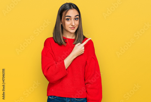Beautiful brunette woman wearing casual winter sweater pointing with hand finger to the side showing advertisement, serious and calm face © Krakenimages.com