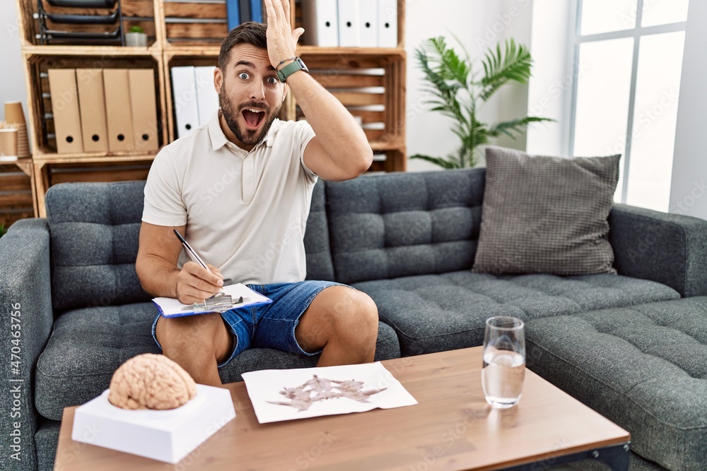 Handsome hispanic man working with rorschach test at psychology clinic surprised with hand on head for mistake, remember error. forgot, bad memory concept. Handsome hispanic man working with rorschach test at psychology clinic surprised with hand on head for mistake, remember error. forgot, bad memory concept.
