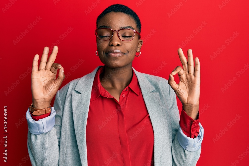 Naklejka premium Young african american woman wearing business jacket and glasses relax and smiling with eyes closed doing meditation gesture with fingers. yoga concept.