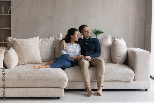 Peaceful 30s couple relaxing on comfortable couch looking out window and daydreaming about bright future at new own house. Bank loan and medical insurance, modern fashionable furniture shop ad concept