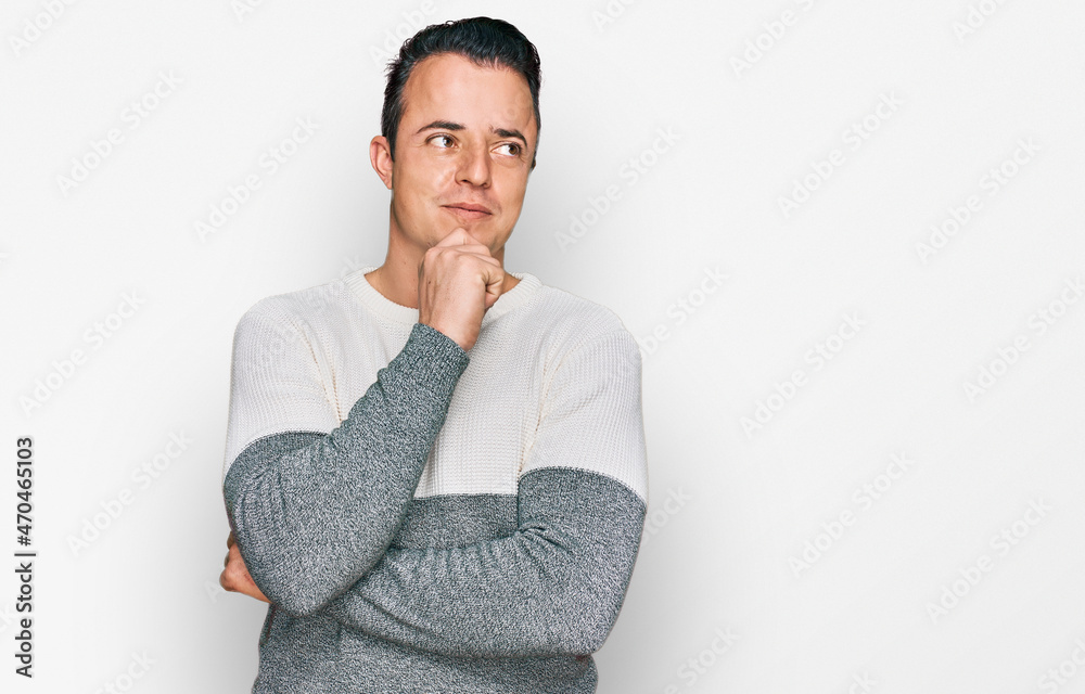 Handsome young man wearing casual winter sweater with hand on chin thinking about question, pensive expression. smiling with thoughtful face. doubt concept. Handsome young man wearing casual winter sweater with hand on chin thinking about question, pensive expression. smiling with thoughtful face. doubt concept.