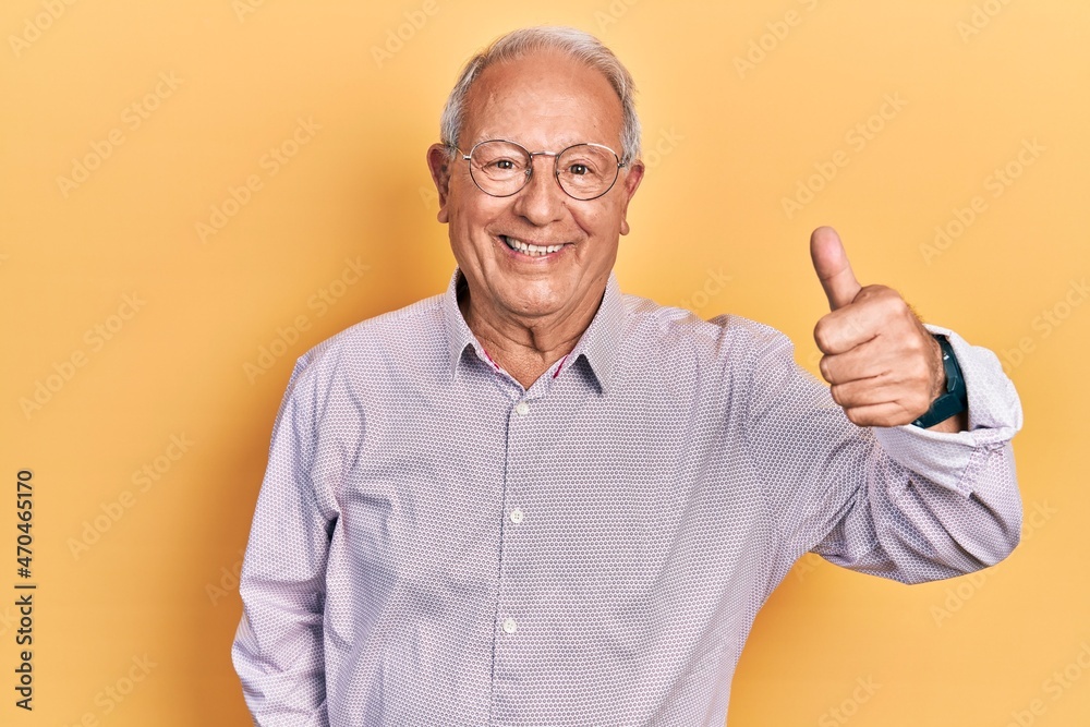 Senior man with grey hair wearing elegant shirt and glasses smiling happy and positive, thumb up doing excellent and approval sign