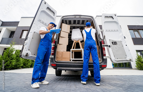 Two removal company workers are loading boxes and furniture into a minibus.