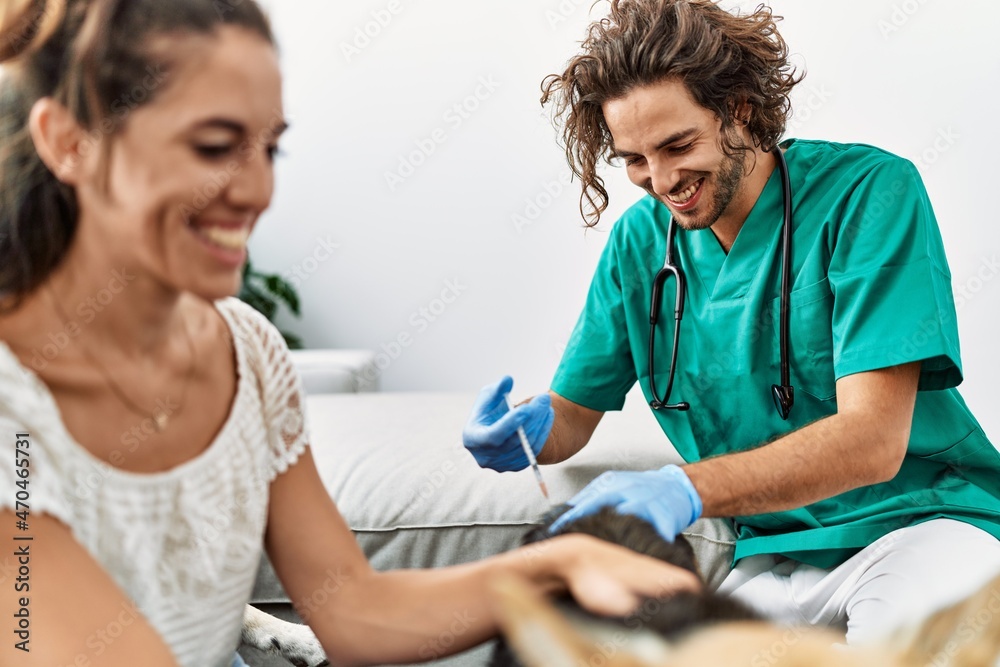 Man and woman wearing veterinarian uniform injecting vaccine to dog at home Man and woman wearing veterinarian uniform injecting vaccine to dog at home