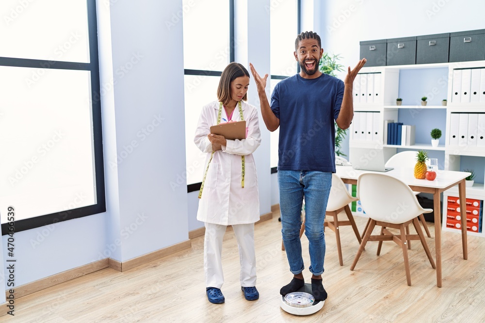Dietitian at the clinic with client checking weight celebrating victory with happy smile and winner expression with raised hands Dietitian at the clinic with client checking weight celebrating victory with happy smile and winner expression with raised hands