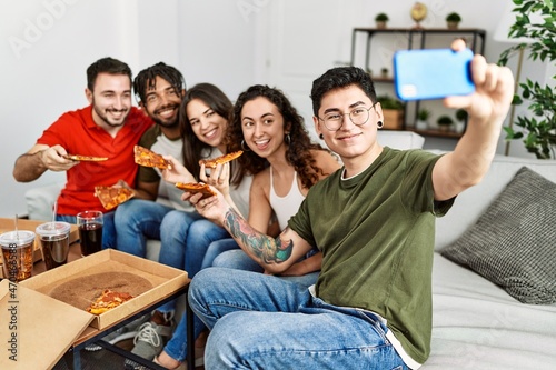 Group of young friends smiling happy eating italian pizza make selfie by the smartphone at home.