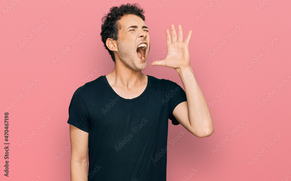 Young handsome man wearing casual black t shirt shouting and screaming loud to side with hand on mouth. communication concept. Young handsome man wearing casual black t shirt shouting and screaming loud to side with hand on mouth. communication concept.