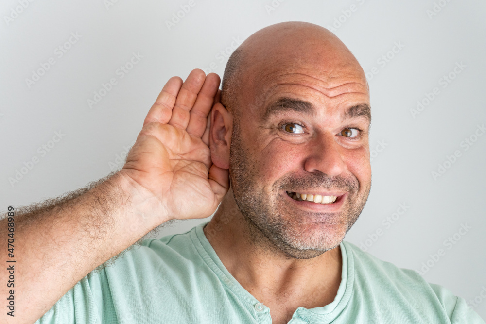 Obraz premium Close-up of the face of a bald, bearded Caucasian man, gesturing with his hand behind his ear.