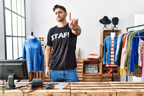 Young hispanic man working at retail boutique pointing with finger up and angry expression, showing no gesture
