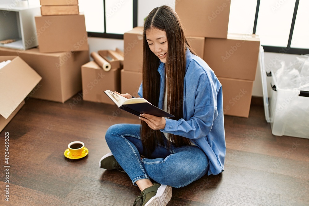 Obraz premium Young chinese girl reading book and drinking coffee at new home