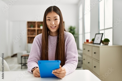 Young chinese girl using touchpad sitting on the table at home.