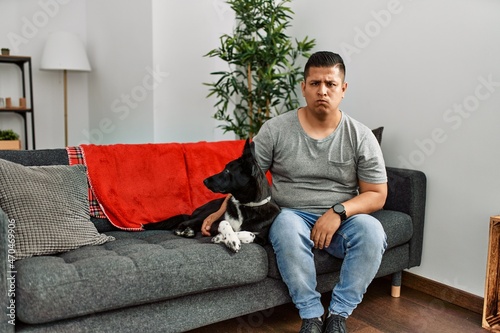 Young latin man and dog sitting on the sofa at home skeptic and nervous, frowning upset because of problem. negative person. © Krakenimages.com