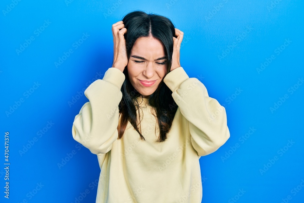 Young brunette woman wearing casual sweatshirt suffering from headache desperate and stressed because pain and migraine. hands on head. Young brunette woman wearing casual sweatshirt suffering from headache desperate and stressed because pain and migraine. hands on head.