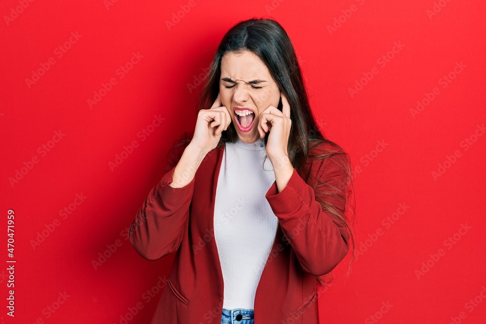 Young brunette teenager wearing business jacket covering ears with fingers with annoyed expression for the noise of loud music. deaf concept.