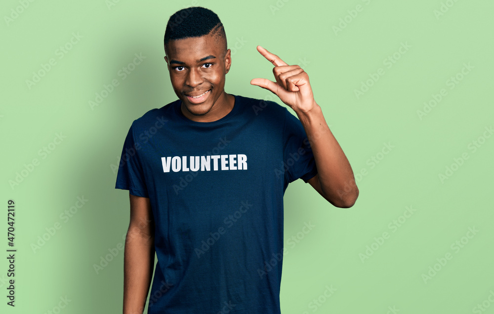 Young african american man wearing volunteer t shirt smiling and confident gesturing with hand doing small size sign with fingers looking and the camera. measure concept. Young african american man wearing volunteer t shirt smiling and confident gesturing with hand doing small size sign with fingers looking and the camera. measure concept.