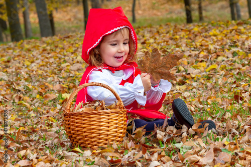 Little Red Riding Hood in the woods with her wicker basket plays with the fallen leaves during the fall.