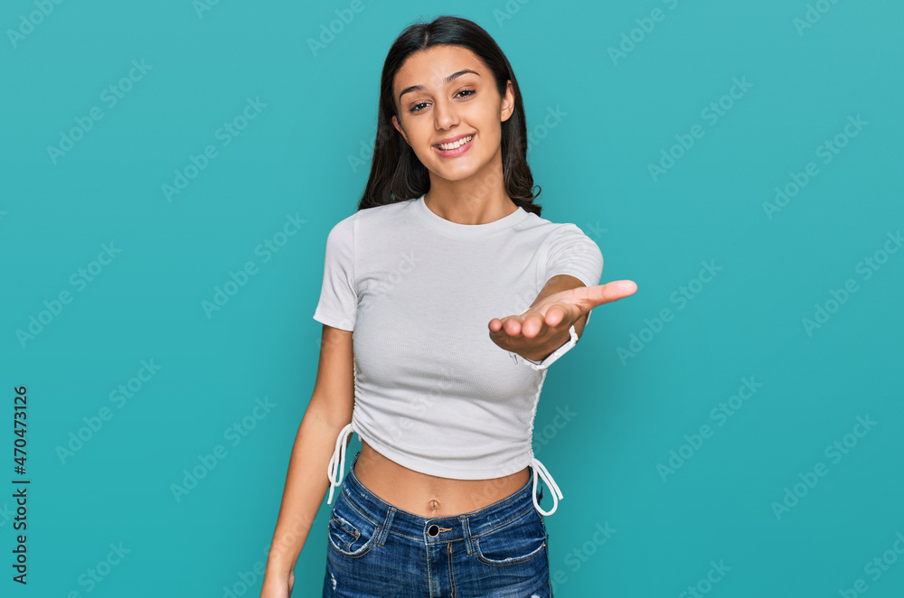 Young hispanic girl wearing casual white t shirt smiling cheerful offering palm hand giving assistance and acceptance. Young hispanic girl wearing casual white t shirt smiling cheerful offering palm hand giving assistance and acceptance.