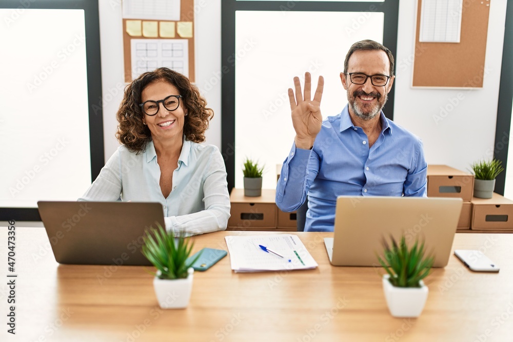 Middle age hispanic woman and man sitting with laptop at the office showing and pointing up with fingers number four while smiling confident and happy. Middle age hispanic woman and man sitting with laptop at the office showing and pointing up with fingers number four while smiling confident and happy.