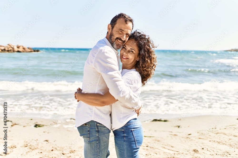 Middle age hispanic couple smiling happy and hugging standing at the beach. Middle age hispanic couple smiling happy and hugging standing at the beach.