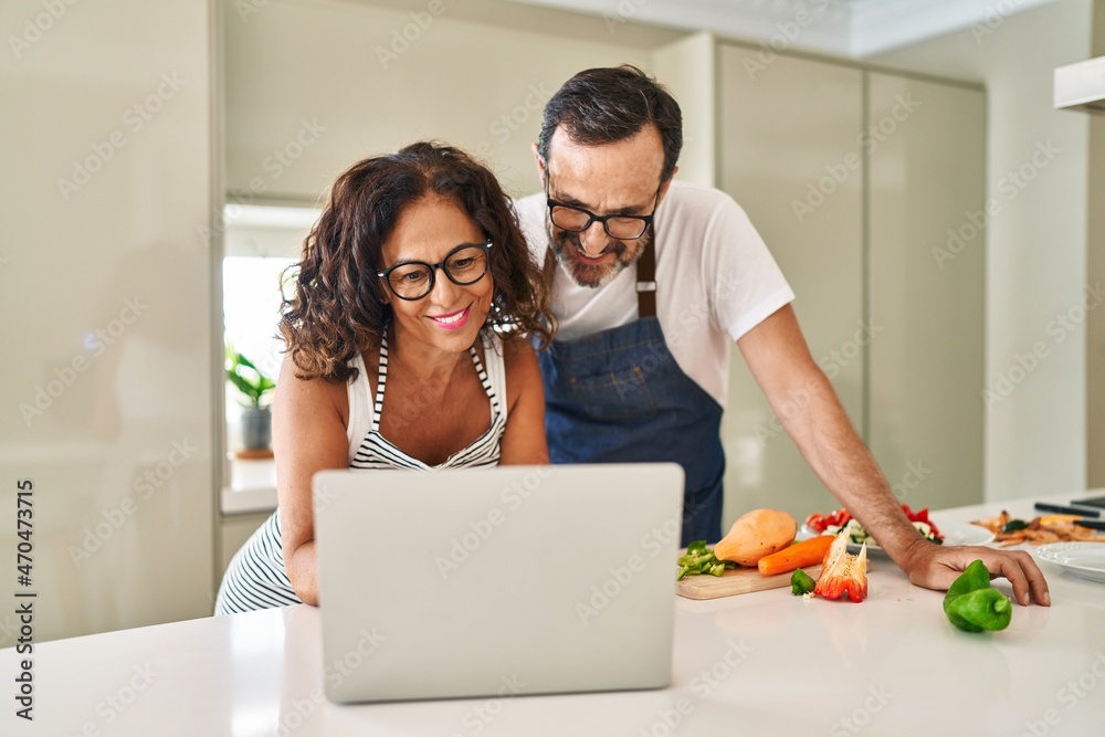 Middle age hispanic couple cooking and using laptop at kitchen Middle age hispanic couple cooking and using laptop at kitchen