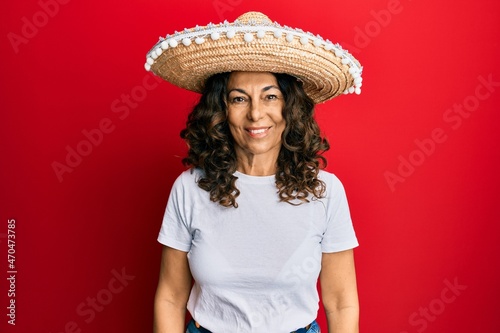 Middle age hispanic woman holding mexican hat looking positive and happy standing and smiling with a confident smile showing teeth © Krakenimages.com