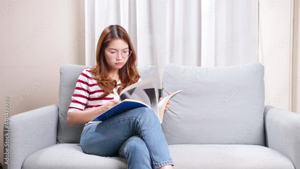 Beautiful young Asian model flipping through picture magazine sitting on sofa at home. Beautiful young Asian model flipping through picture magazine sitting on sofa at home.