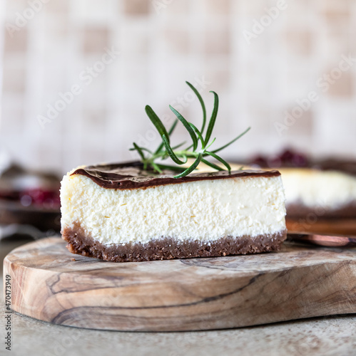 Piece of classic homemade cheesecake with dark chocolate topping and rosemary, concrete background.