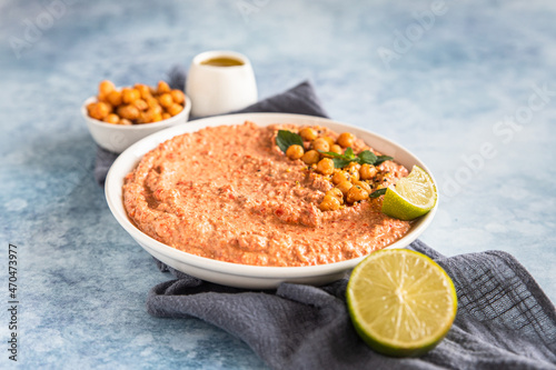 Roasted red pepper hummus garnish with mint and lime. Mashed chickpeas with red bell pepper, lime and mint. Vegetarian snack.