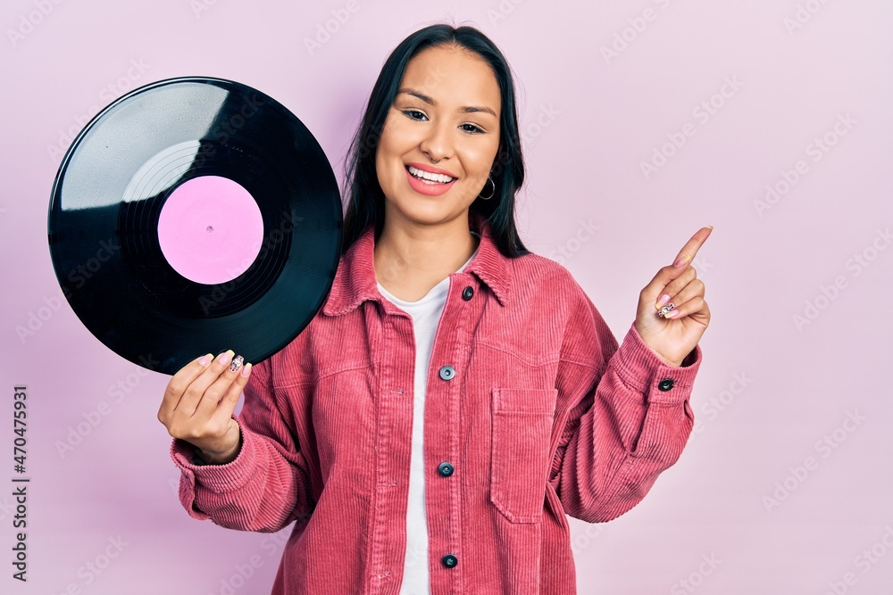 Beautiful hispanic woman with nose piercing holding vinyl disc smiling happy pointing with hand and finger to the side Beautiful hispanic woman with nose piercing holding vinyl disc smiling happy pointing with hand and finger to the side