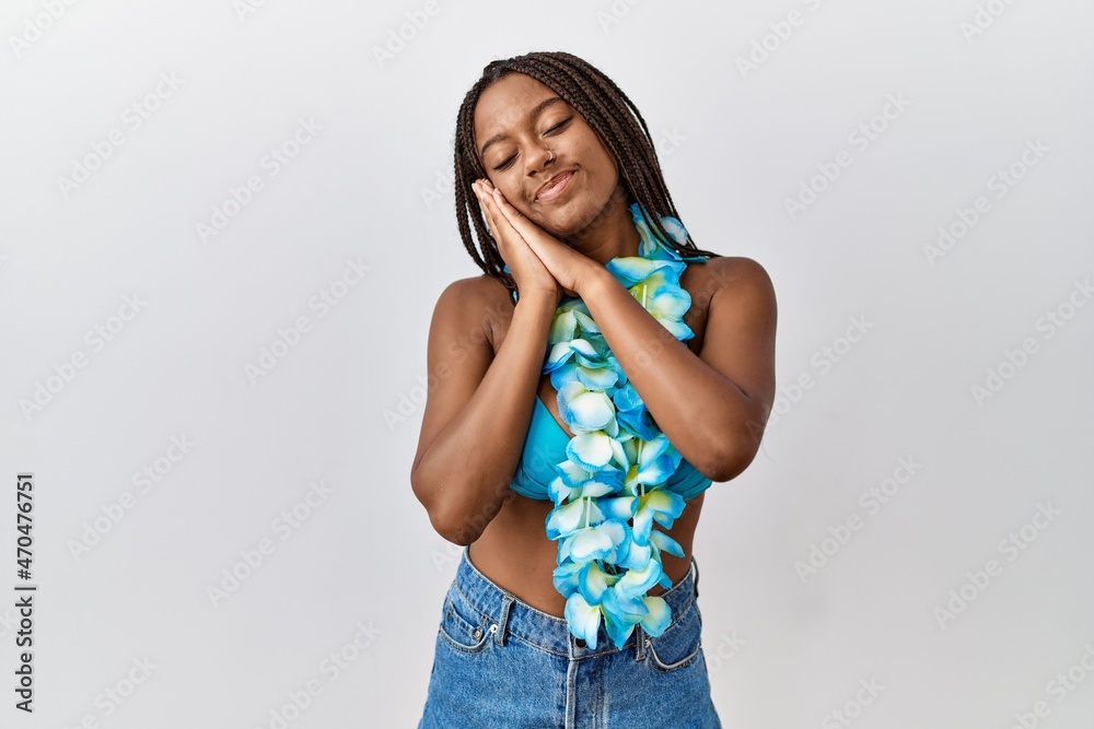 Young african american woman with braids wearing bikini and hawaiian lei sleeping tired dreaming and posing with hands together while smiling with closed eyes. Young african american woman with braids wearing bikini and hawaiian lei sleeping tired dreaming and posing with hands together while smiling with closed eyes.