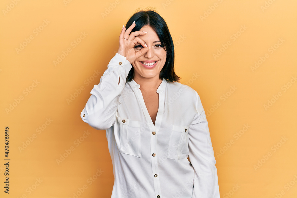 Young hispanic woman wearing casual clothes doing ok gesture with hand smiling, eye looking through fingers with happy face. Young hispanic woman wearing casual clothes doing ok gesture with hand smiling, eye looking through fingers with happy face.