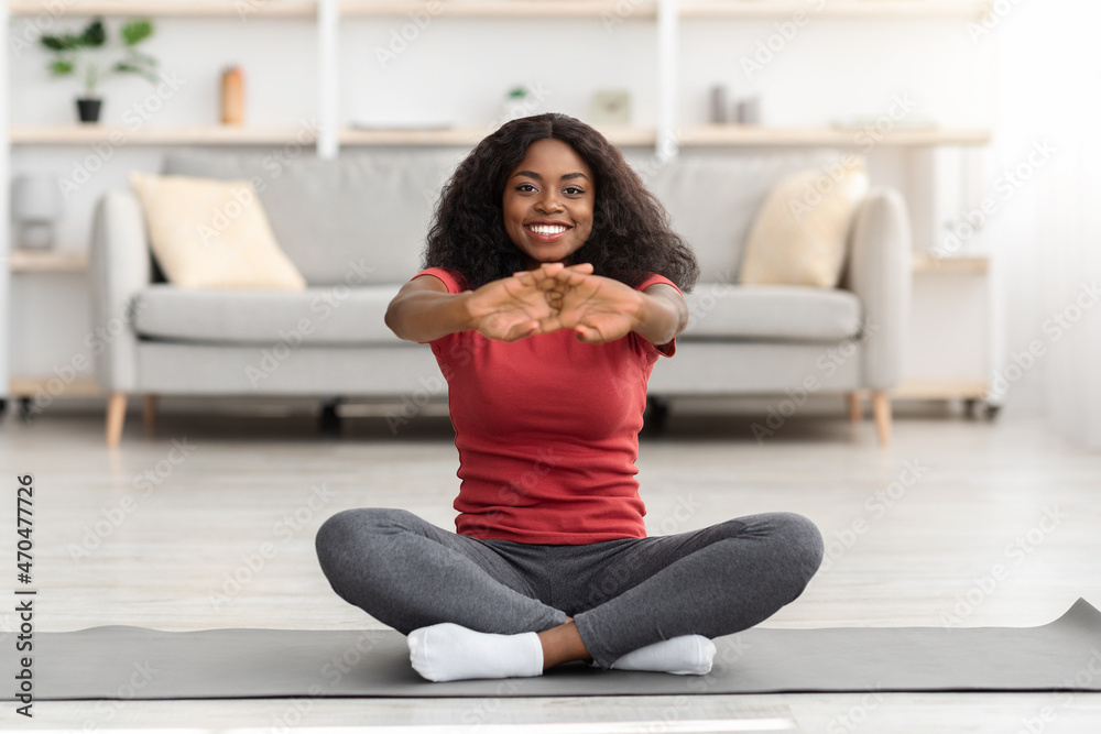 Cheerful african american athletic woman stretching her body at home