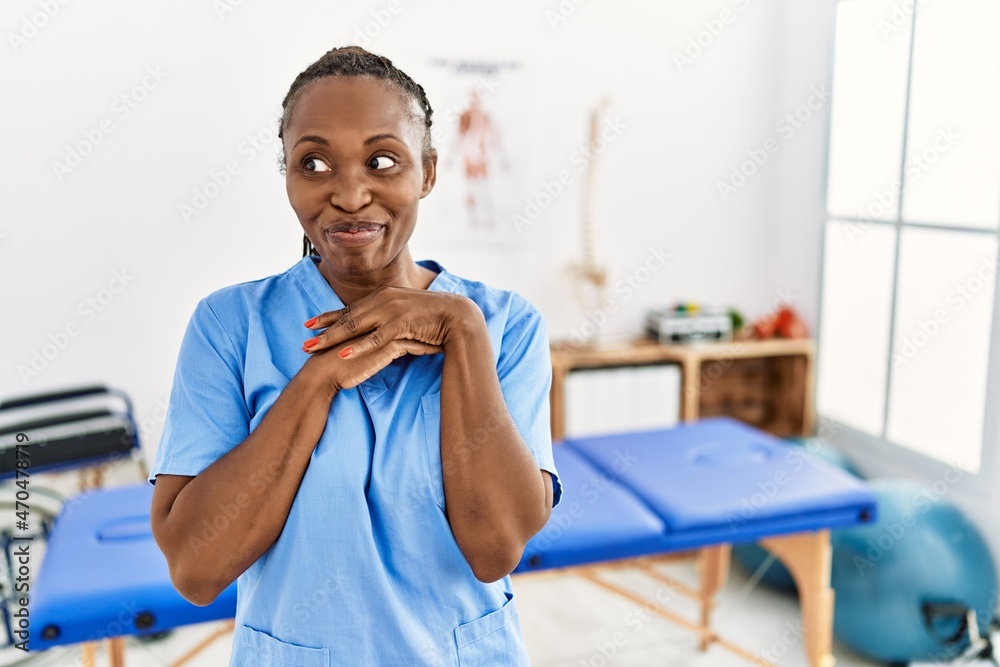 Black woman with braids working at pain recovery clinic laughing nervous and excited with hands on chin looking to the side Black woman with braids working at pain recovery clinic laughing nervous and excited with hands on chin looking to the side