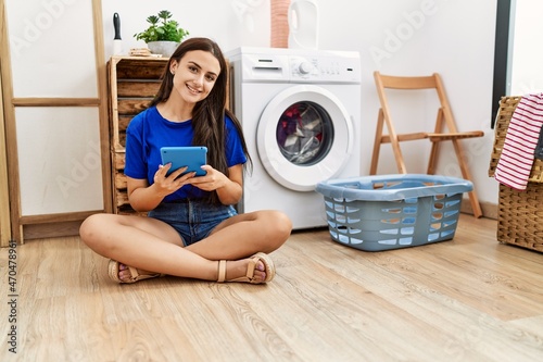 Young caucasian woman using touchpad waiting for washing machine at laundry room
