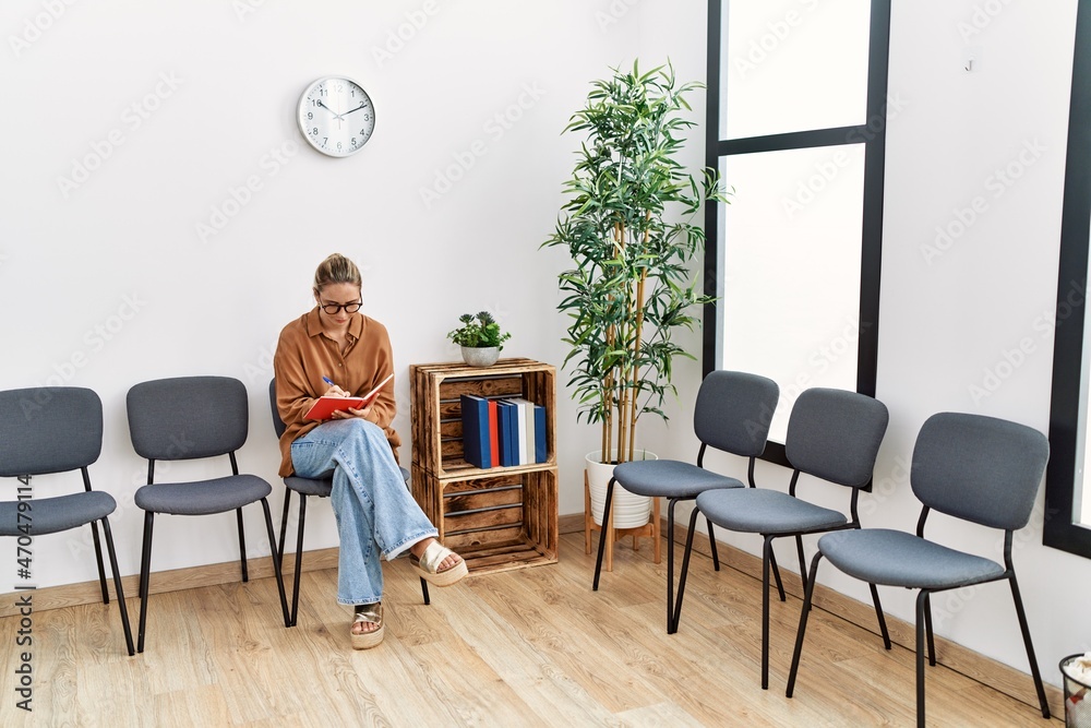 Young blonde woman writing on notebook at waiting room Young blonde woman writing on notebook at waiting room