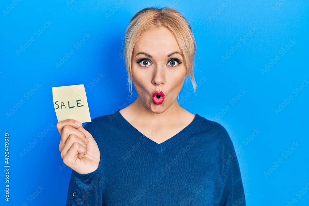 Young blonde woman holding sale word reminder scared and amazed with open mouth for surprise, disbelief face Young blonde woman holding sale word reminder scared and amazed with open mouth for surprise, disbelief face