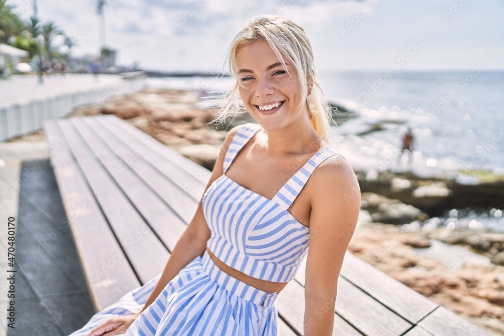 Young blonde girl smiling happy sitting on the bench at the beach.