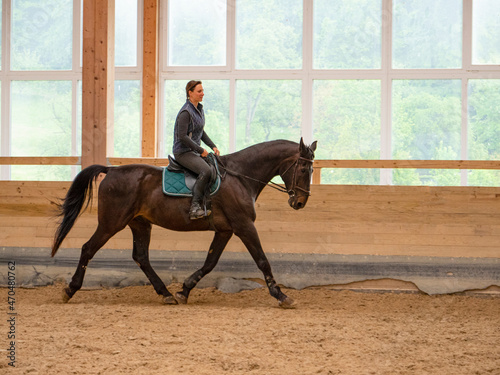 Young Caucasian woman is horseback riding indoors as training for competition.
