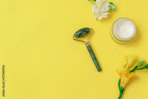 Flat lay with jade roller and flowers on yellow background. Image with copy space, top view © Elena