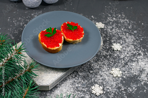 Red caviar on bread in a gray plate, a festive snack of sandwiches on a gray background with snowflakes. Composition of Christmas and New Year holidays.