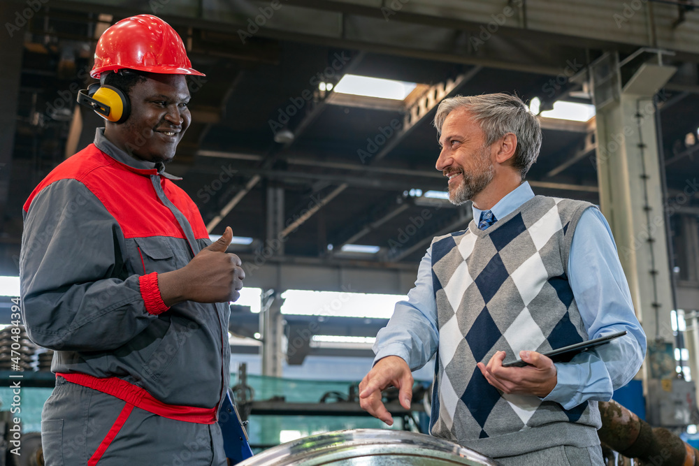 Smiling Manager Talking To African American Worker In Protective Workwear At Train Factory - Multiracial Industrial Co-Workers Standing Next To Train Wheels. Smiling Black Worker Giving Thumb Up Smiling Manager Talking To African American Worker In Protective Workwear At Train Factory - Multiracial Industrial Co-Workers Standing Next To Train Wheels. Smiling Black Worker Giving Thumb Up