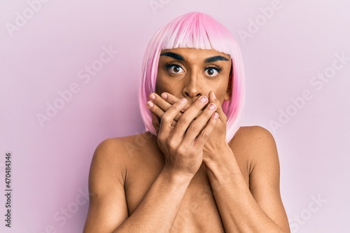 Hispanic transgender man wearing make up and pink wig shocked covering mouth with hands for mistake. secret concept.