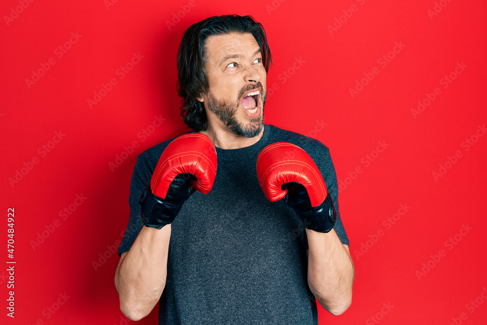 Middle age caucasian man using boxing gloves angry and mad screaming frustrated and furious, shouting with anger. rage and aggressive concept. Middle age caucasian man using boxing gloves angry and mad screaming frustrated and furious, shouting with anger. rage and aggressive concept.