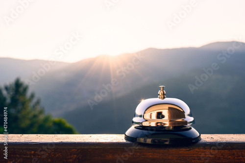 Silver vintage bell on village reception desk in the morning sunrise mountain. Eco, camping hotel service, registration.