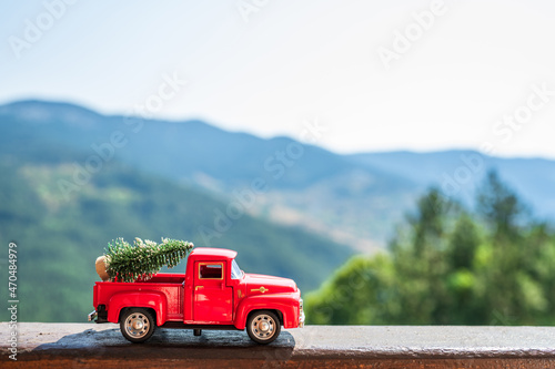 Red retro small car carrying christmas tree in the mountain. Winter holiday concept