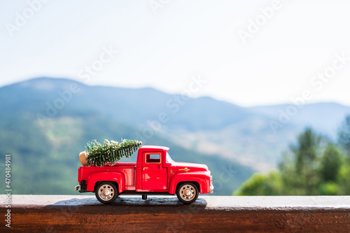 Red retro small car carrying christmas tree in the mountain. Winter holiday concept