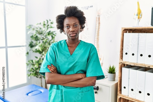 African young physiotherapist woman working at pain recovery clinic relaxed with serious expression on face. simple and natural looking at the camera.
