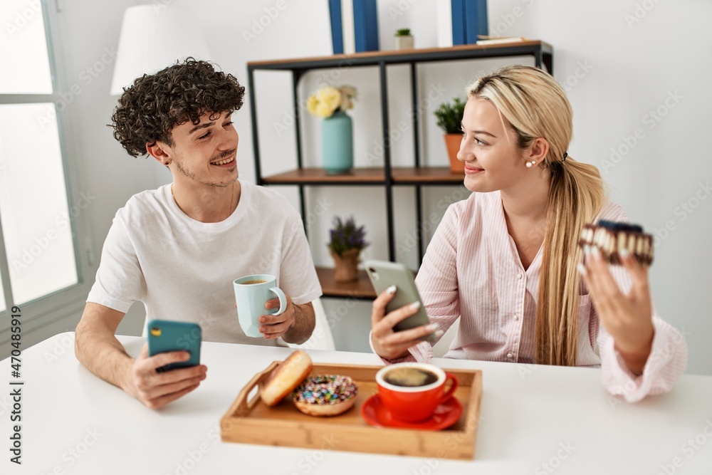 Young couple having breakfast using smartphone at home.